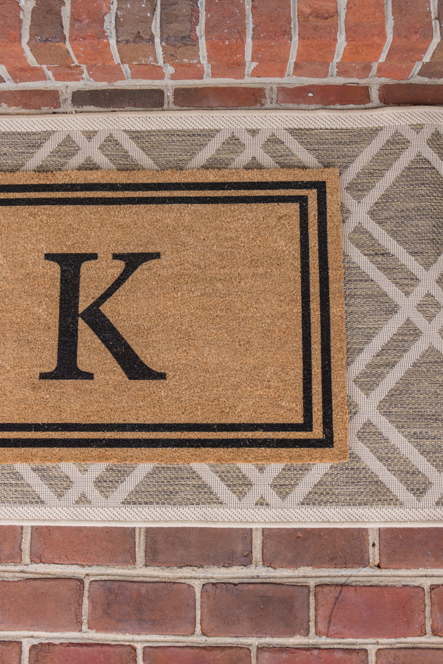 Arched manor spring front porch styling, close-up image of initial doormat layered and styled over a neutral print rug
