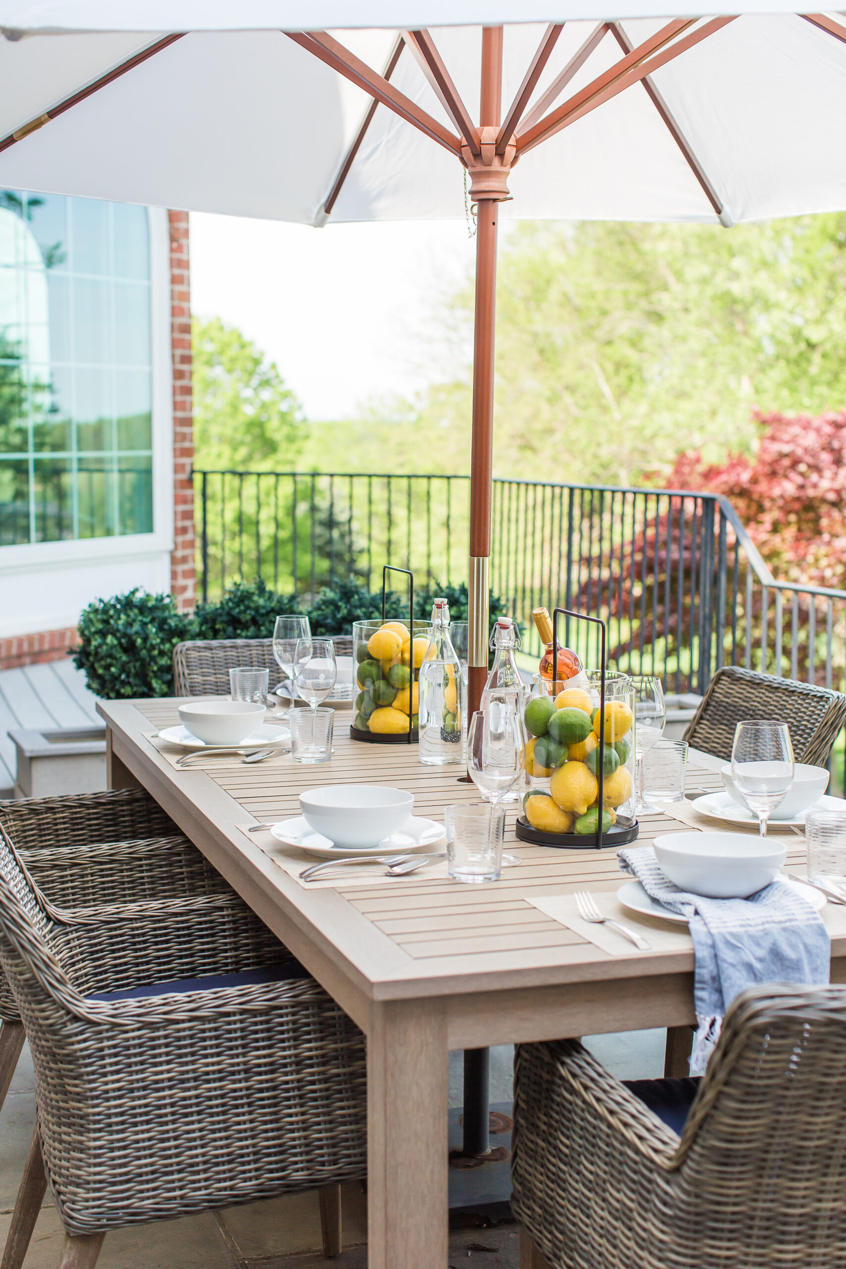 close up of outdoor patio dining table styling with a patio umbrella, wicker patio chairs, artificial lemons and limes decorated in candle lanterns