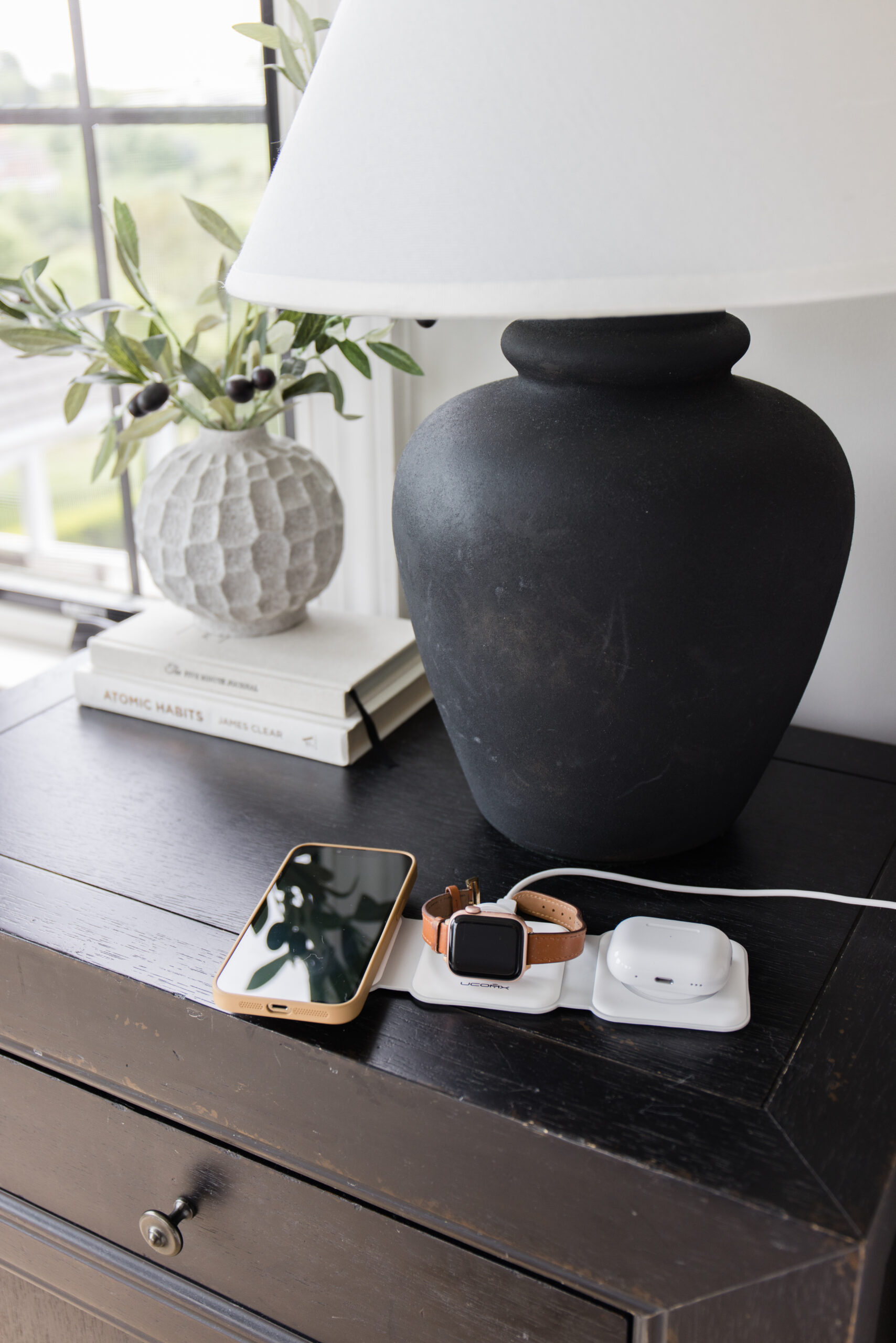 charging phone and Apple watch on nightstand with 3-in-1 Charging Station next to black lamp with off white vase styled with faux olive stems