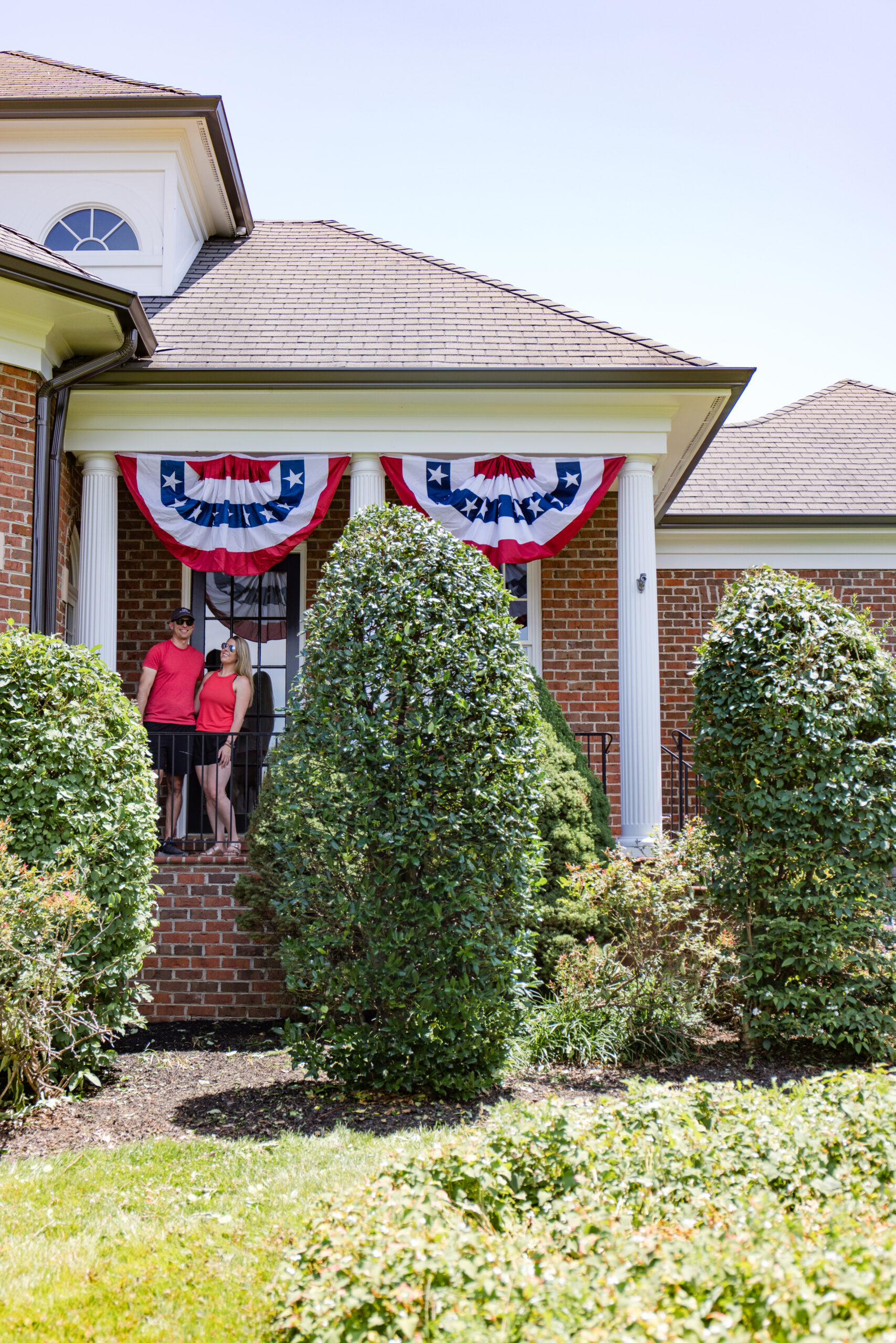 john and megan standing on the arched manor porch with American bunting flags hanging